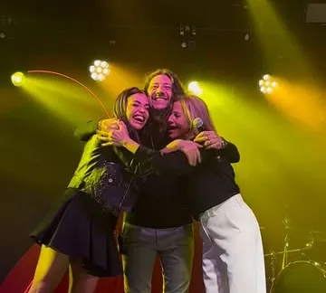 Facundo Toro abrazado con dos cantantes sobre el escenario, bajo luces amarillas