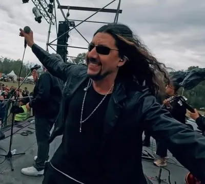 Cantante de Los Nombradores del Alba con anteojos de sol, brazos abiertos frente al público de un festival